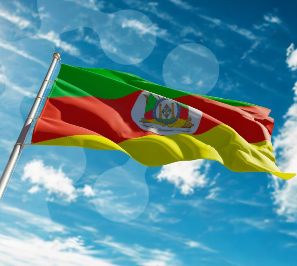 Bandeira do Rio Grande do Sul tremulando ao vento sob um céu azul com nuvens.